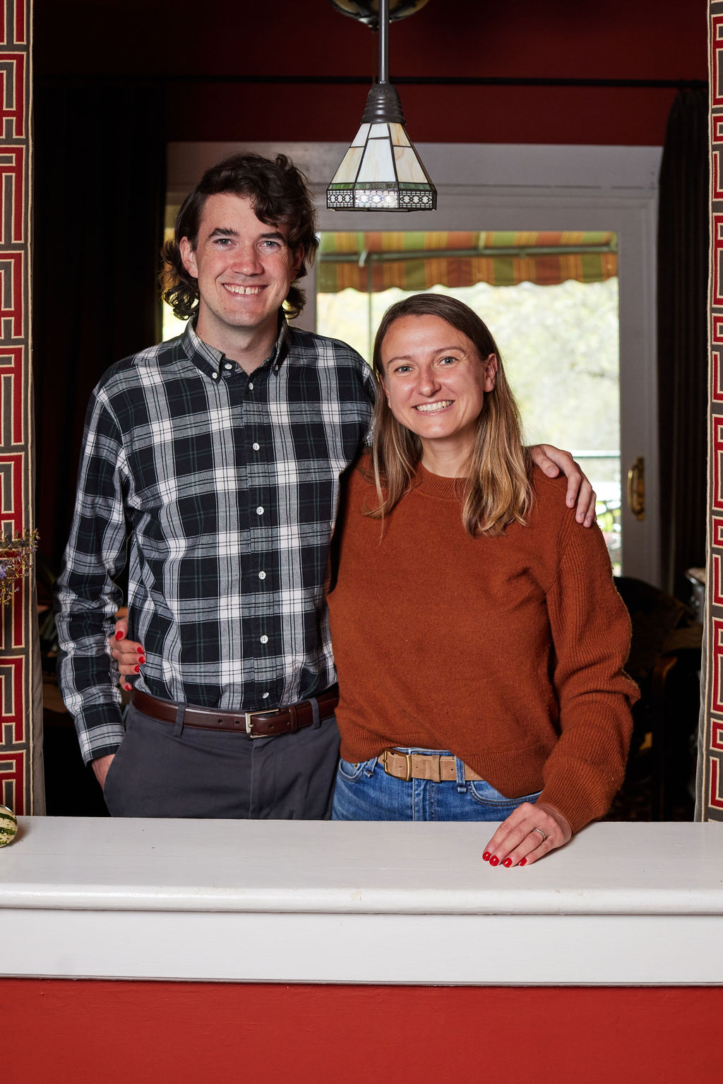 Claire and Toph, smiling at the camera, Toph’s arm lovingly around Claire’s shoulder, standing at the top of the Apple Tree hill in front of the unseen old carriage house, a beautiful verdant backdrop with layered mountains and just a hint of the Stockbridge Bowl visible at the far right
